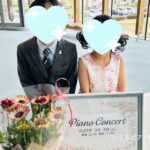 いぐちピアノ教室の看板の前でポーズを決めている生徒さんの画像